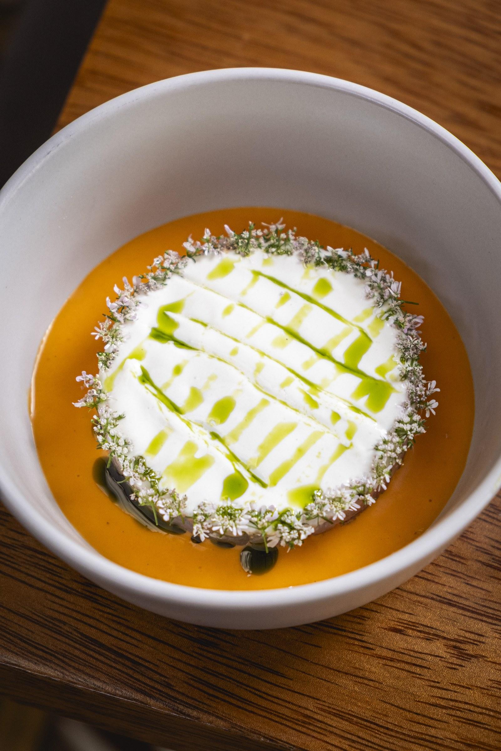 Crema anaranjada con espuma blanca, aceite de hierbas y flores