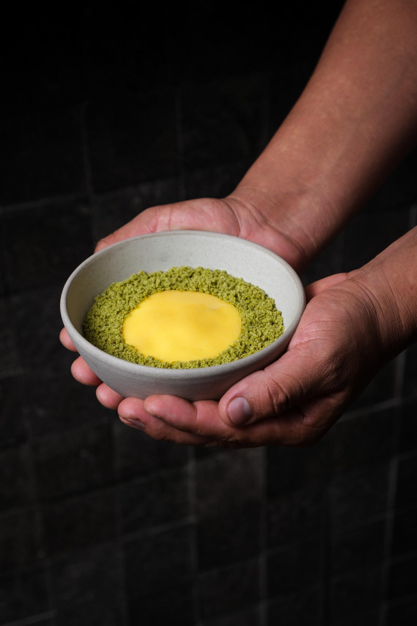 Manos sosteniendo un bowl con crema amarilla y crocante verde